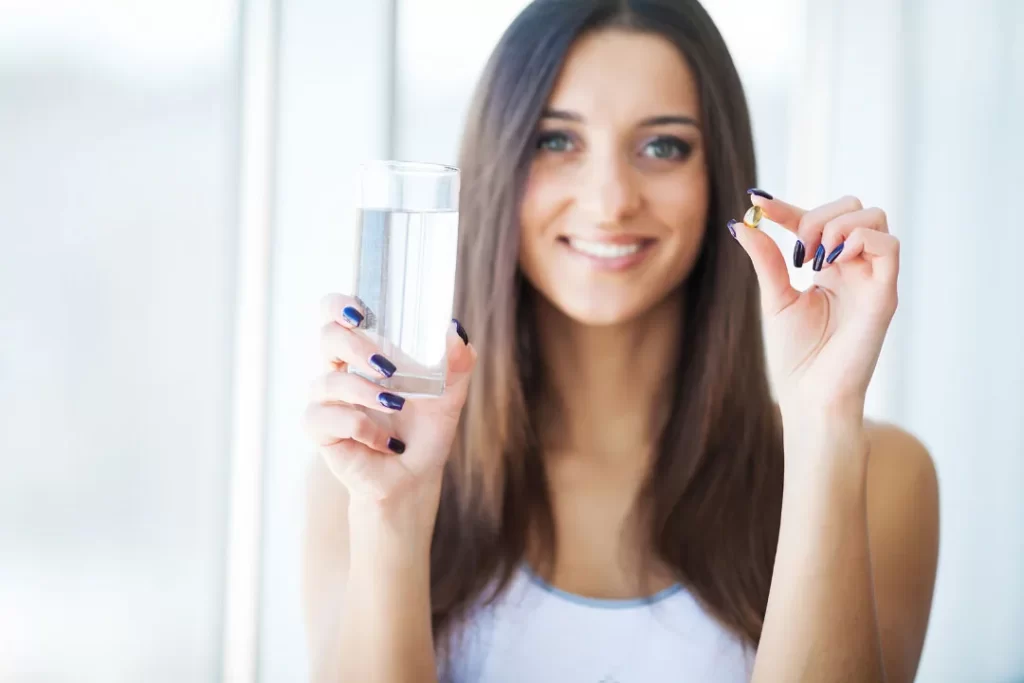 A girl taking supplement with a glass of water.