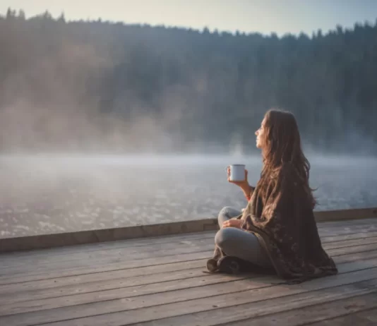 Young woman relaxing near lake beach and drinking mushroom drink